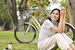 Happy and relaxed Asian woman listening to music and taking a rest after cycling in the public park