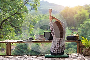 Happy relaxed asian young woman sitting in the midst of nature with a laptop in the back of her stretching her arms above her head photo