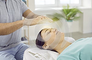 Happy relaxed and calm young woman with closed eyes receiving reiki treatment above head.