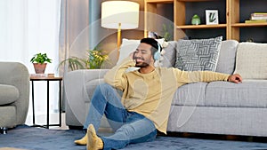 Happy relaxed man listening to music using headphones while sitting on the floor of his house. Young male relaxing at