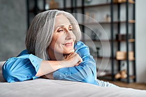 Happy relaxed mature old woman resting dreaming sitting on couch at home.