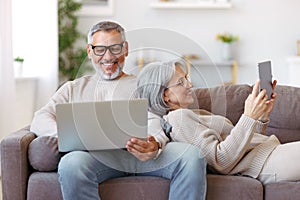 Happy relaxed old retired family couple using modern technologies laptop and digital tablet at home