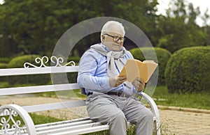 Happy relaxed senior man resting reading an interesting book sitting on a park bench.