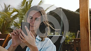 Happy relaxed tourist woman resting in beach lounge chair using smartphone entertainment app on exotic vacation resort.