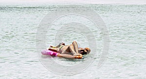 Happy and relaxed woman with bikini lay down on a coloured lilo at the beach enjoying the blue transparent amazing water in summer