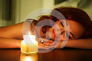 Happy relaxed woman enjoying the aroma of candle. Smiling girl looks at a burn candle in home cosiness in the evening