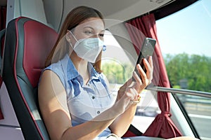 Happy relaxed woman with KN95 FFP2 face mask using smart phone on public transport. Bus passenger with protective mask texting on