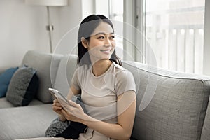 Happy relaxed young Asian woman using cellphone at home