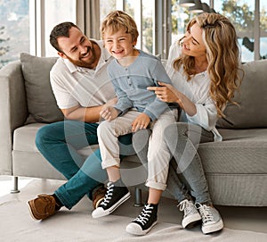 Happy relaxing caucasian family of three smiling while sitting and bonding on the sofa together. Adorable little blonde