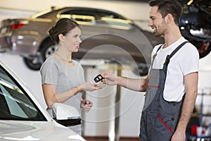 Happy repairman giving car key to woman in workshop