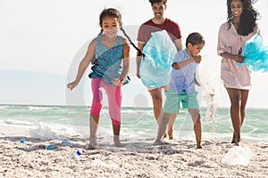 Happy responsible multiracial family collecting plastic garbage from sand at beach on sunny day