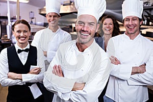 Happy restaurant team standing together with arms crossed in commercial kitchen