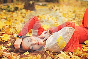 Happy resting girl portrait, lying in autumn maple leaves in park, closed eyes, dressed in fashion sweater