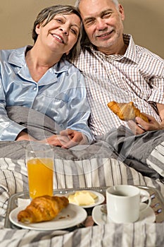 Happy retired couple eating croissant breakfast