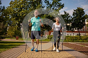 Happy retired couple enjoying pole walk training in urban public park