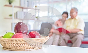 Happy retired couple reading book on a couch in living room with fresh fruit on the table to healthy eating and lifestyle