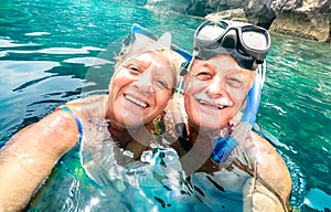 Happy retired couple with scuba mask taking selfie at tropical excursion - Boat trip snorkel experience in exotic scenarios