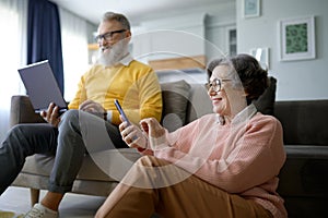 Happy retired couple using digital gadget while resting at home