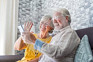 Happy retired family couple using mobile phone for video call together, talking to relations, getting good news, having fun,