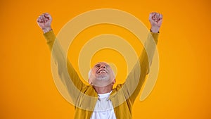 Happy retired man stretching hands up, celebrating success on orange background