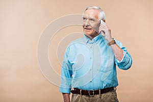 happy retired man talking on smartphone and standing isolated on beige.