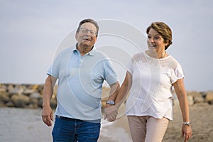 Happy retired mature couple walking on the beach - pensioner woman and her husband taking romantic walk together enjoying sweet