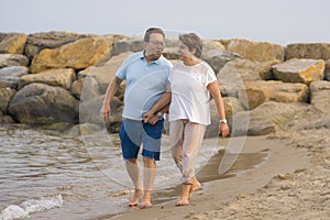 Happy retired mature couple walking on the beach - pensioner woman and her husband taking romantic walk together enjoying sweet