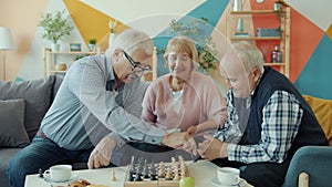 Happy retired men playing chess game while cheerful woman watching and smiling