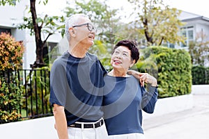 Happy retired senior Asian couple walking and looking at each other with romance in outdoor park and house in background.