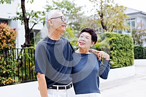 Happy retired senior Asian couple walking and looking at each other with romance in outdoor park and house in background. photo