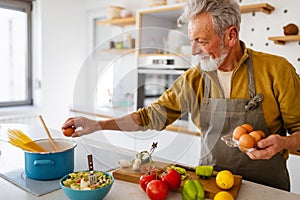 Happy retired senior man cooking in kitchen. Retirement, hobby people concept