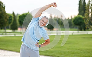 Happy retired senior man doing side stretching exercises with arm overhead during outdoor workout