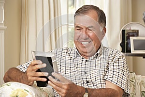 Happy Retired Senior Man Sitting On Sofa At Home Looking At Photograph