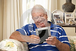 Happy Retired Senior Man Sitting On Sofa At Home Looking At Photograph