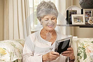 Happy Retired Senior Woman Sitting On Sofa At Home Looking At Photograph