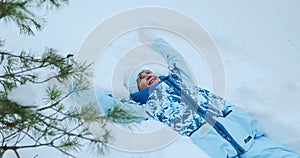 A happy retired woman lies in the snow in a winter forest and makes a snow angel