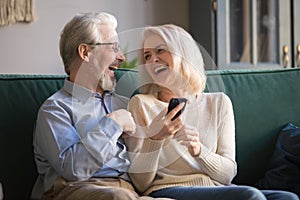 Happy retirees family laughing using smartphone at home.