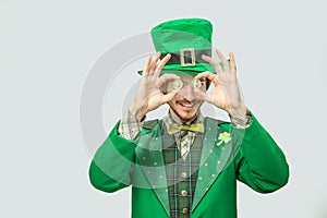 Happy rich young man in green suit hold two golden coins in front of eyes. He smile and look happy. Guy wear green saint