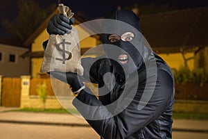 Happy robber or burglar is showing stolen bag full of money at night