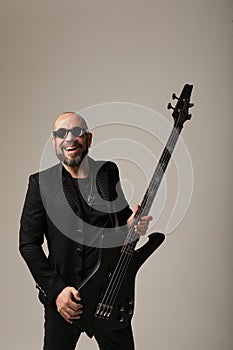Happy rock musician. A man with shaved head and electric guitar poses indoor.