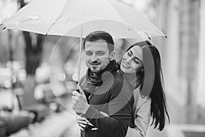 Happy romantic couple, guy and his girlfriend dressed in casual clothes are hugging under the umbrella and look at each