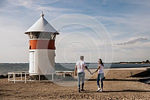 Happy romantic couple hold hands and walk on the beach with lighthouse