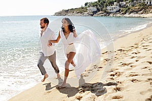 Happy romantic couple hold their hands and go on the beach in Greece, the honeymoon vacation, sunny day in the summer.