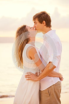 Happy romantic couple kissing on the beach at sunset