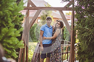 Happy romantic couple in the village, stroll on the wooden bridge. Young beautiful woman in long summer dress hugging