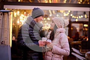 Happy romantic couple wearing warm clothes enjoying spending time together on a date in evening street near a cafe