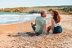 Happy romantic couple woman and man sitting on the beach near the sea and hug each other