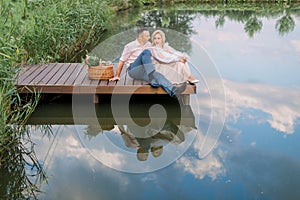 Happy romantic mature couple sitting on a wooden bridge near lake or pond outdoors