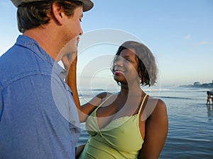 Happy and romantic mixed race couple with attractive black African American woman and Caucasian man playing on beach having fun