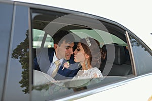 Happy romantic newlyweds, bride and groom kissing in wedding car